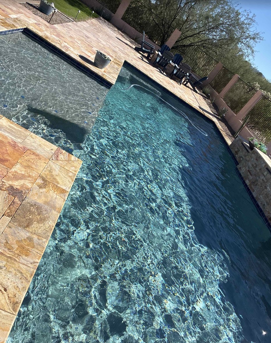 Pool Services Clear blue backyard swimming pool with a shallow sun shelf and stone patio